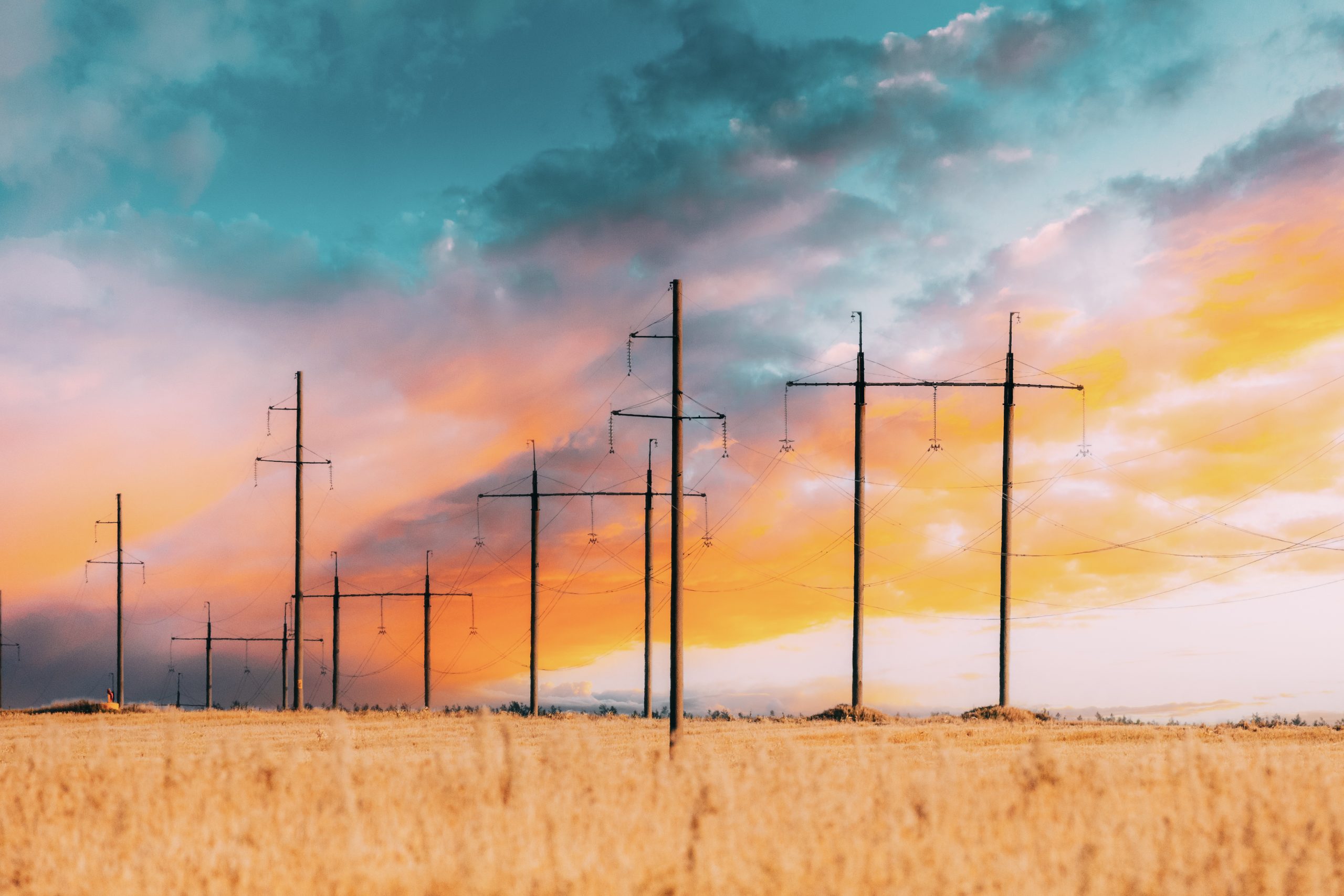 Harvest Field Under Power Line Background. Harvest Field Combination Nature And Technologie. Bright Colors. Fiery Sunset Clouds Sky. Yellow, Orange, Blue Colors. Sunlight Shining Through Clouds.